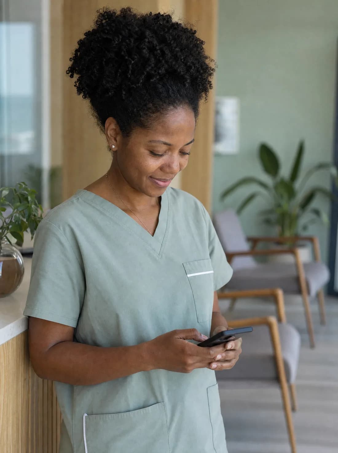 Profissional de saúde em pé na recepção do próprio consultório, sorrindo ao ler uma mensagem no celular