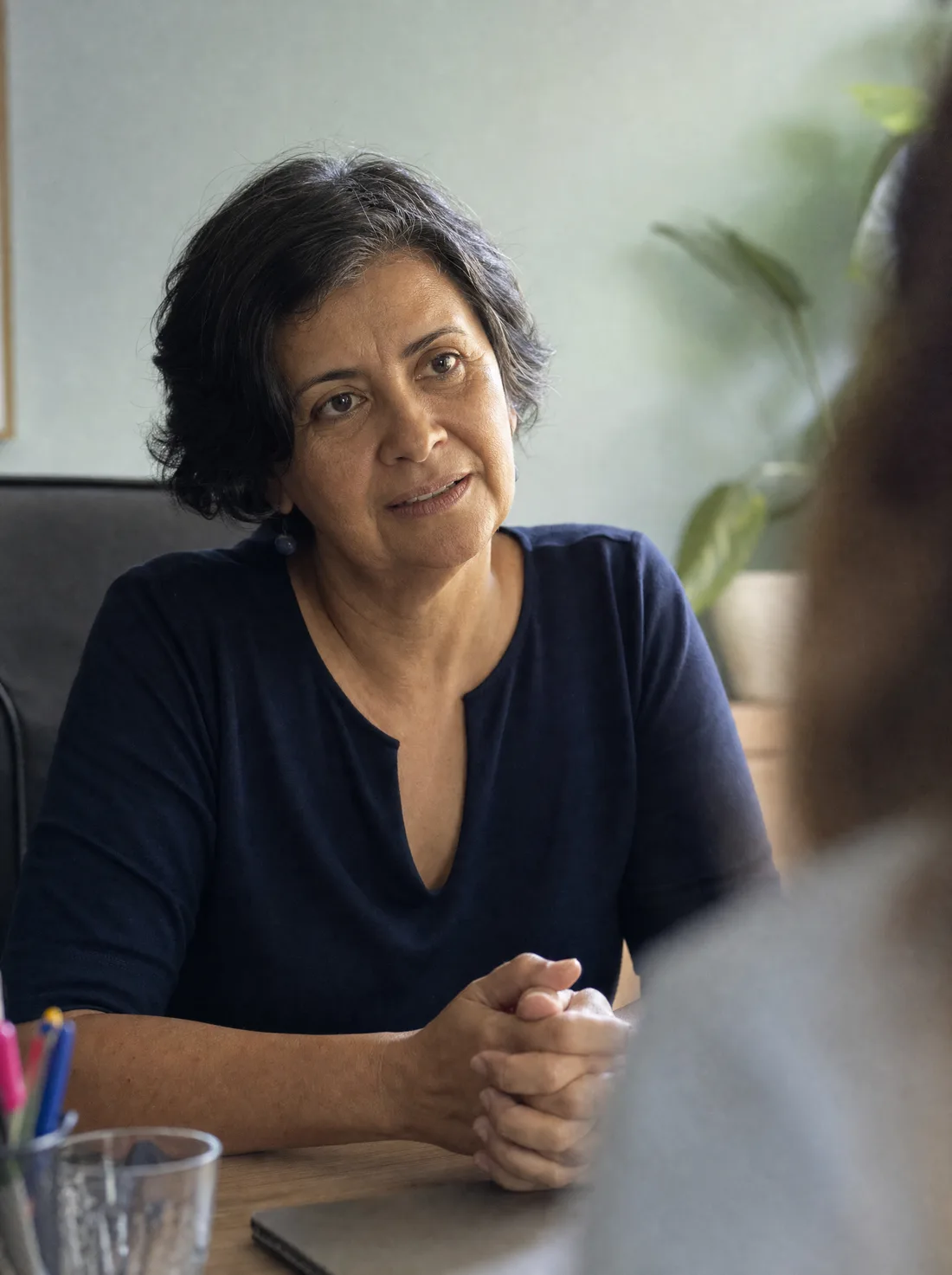 Médica sentada à mesa do consultório em conversa com alguém fora do enquadramento