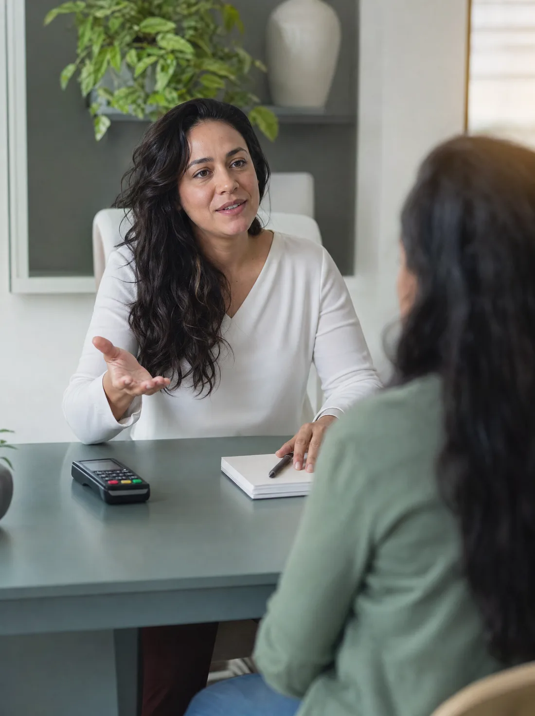 Profissional à mesa do consultório combinando as condições de atendimento com alguém fora do enquadramento